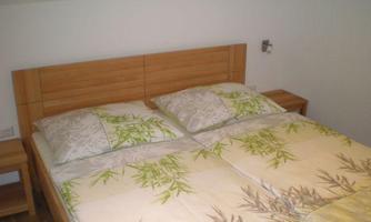 A cozy bedroom with a double bed and wooden details. The bedding has a green plant pattern.