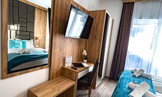 A modern hotel room with a comfortable bed and a desk. The walls are in wood look and there are large windows with daylight.