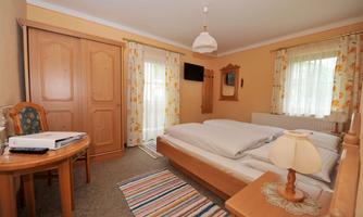 A bright room with a double bed and a wooden table. The room has large windows, a cozy decor, and a carpet.