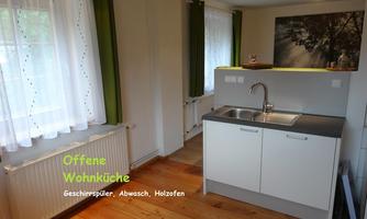 A bright, open kitchen with a wooden floor. It is modernly equipped with a sink and a window that lets in daylight.