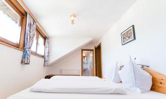 A cozy bedroom with two beds and large windows. The room is bright and cheerfully decorated.