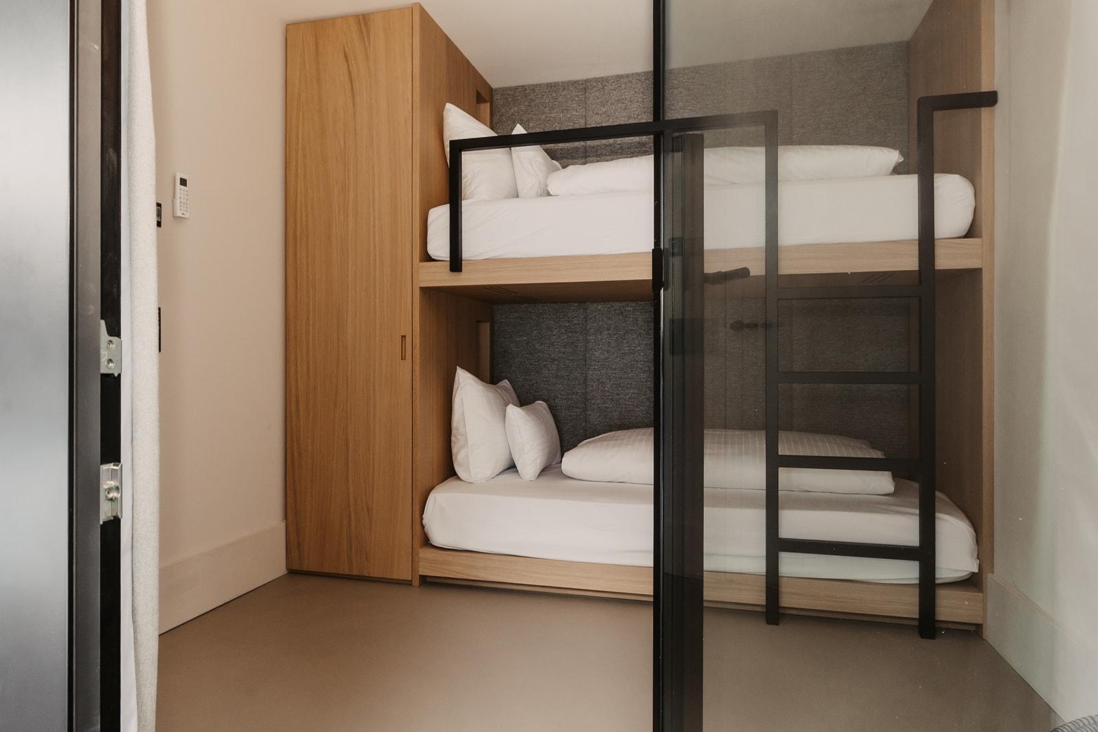 A modern room with a wooden bunk bed. The walls are kept neutral and the floor is simple and bright.