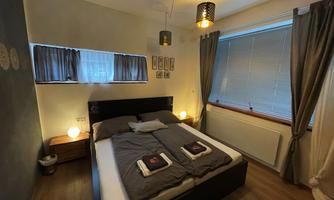 A cozy bedroom with a double bed and modern lamps. Large windows and warm colors create an inviting atmosphere.