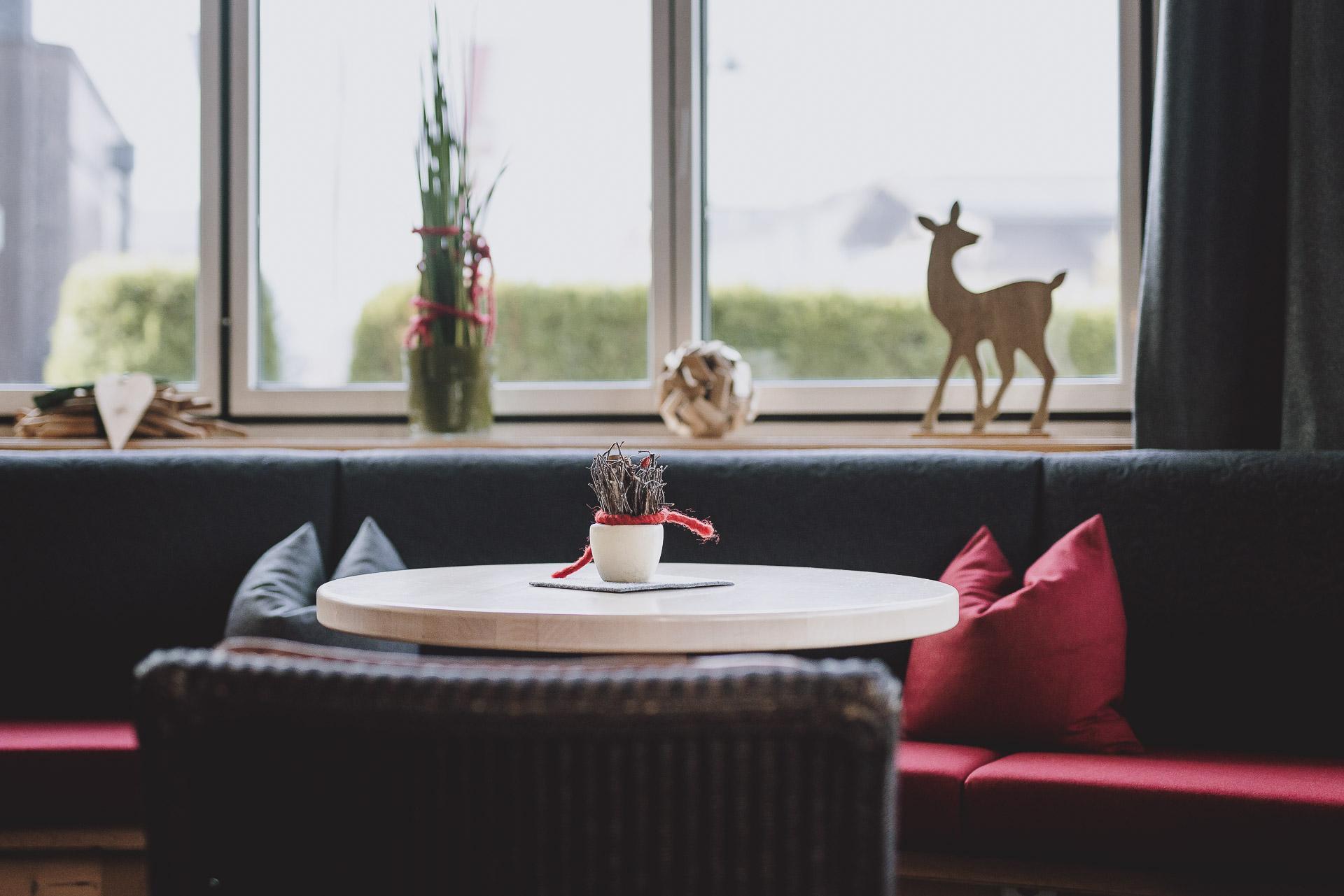 A cozy room with a round table and colorful cushions. In the background, there is a small decoration with a wooden deer figure.