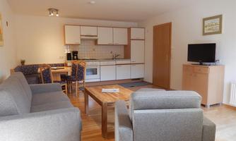 A modern living room with a cozy sofa and a dining table. The kitchen is open and well-equipped.