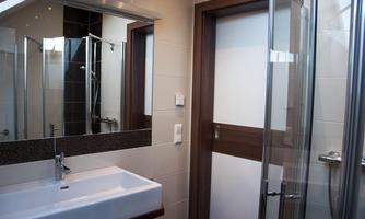 A modern bathroom with a sink, mirror, and a glass-enclosed shower. The walls are brightly tiled, and there are wooden accents.