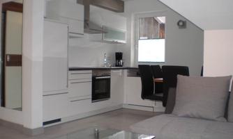 A modern kitchen with white furniture and a dining area. The space is bright and inviting, with a large window.