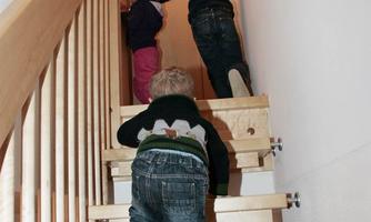 Three children are climbing a staircase. They are on their way to a door at the end of the hallway.