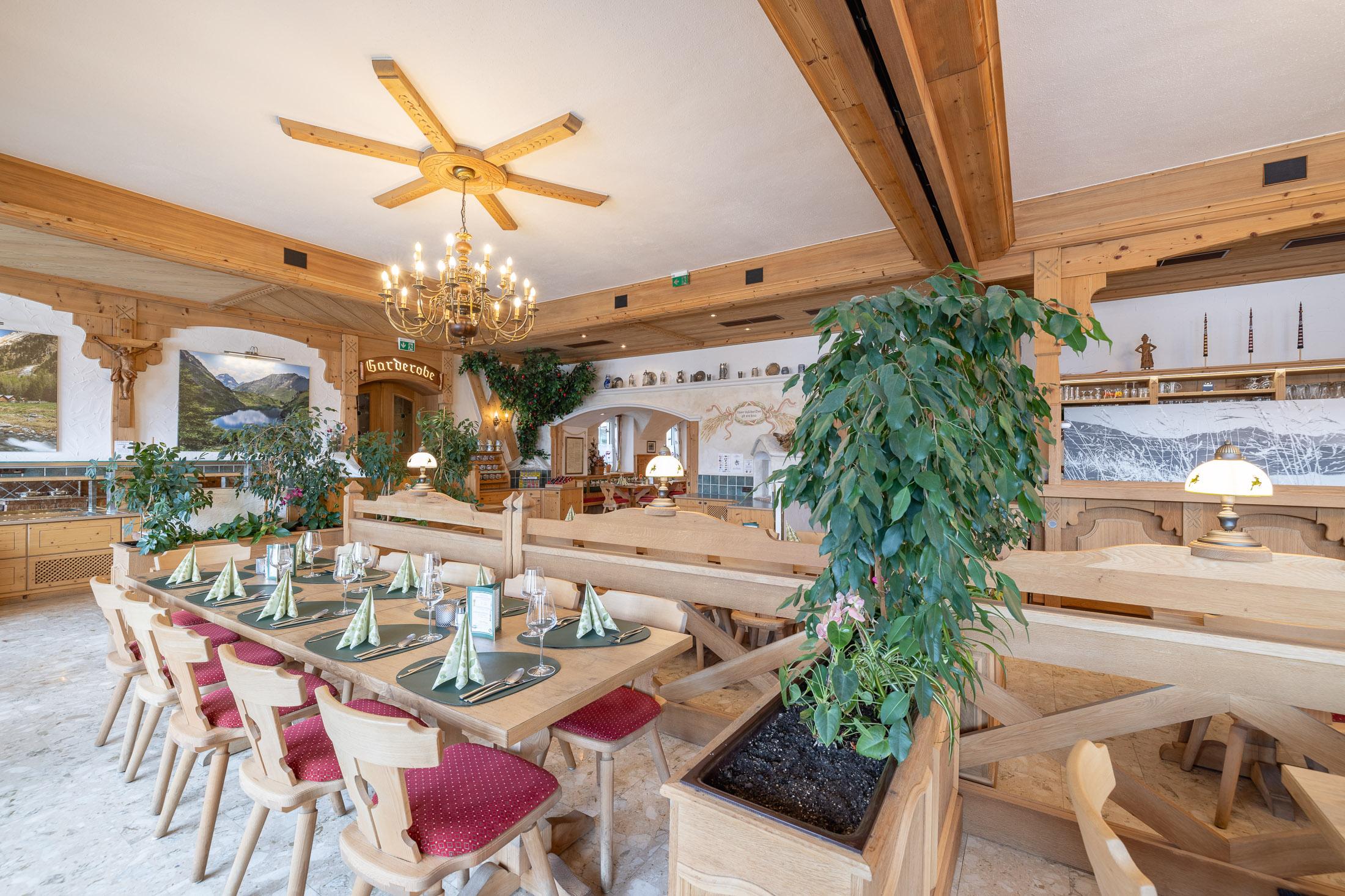 A cozy dining room with wooden tables and chairs. Plants and a rustic decor create an inviting atmosphere.