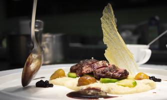 An artistically arranged dish with tender meat, puréed vegetables, and decorative elements. The presentation showcases a combination of colors and textures.