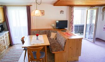A cozy living kitchen with a dining area and a view of a balcony. The room is bright and cheerfully furnished.