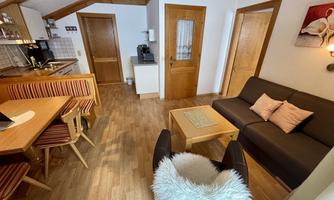 A cozy apartment with an open kitchen and dining area. The living space is furnished with a comfortable sofa and a wooden table.