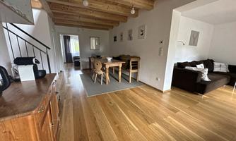 A bright and open living area with wooden floors and ceiling. There is a dining area with a table and chairs, as well as a cozy seating area with a sofa.