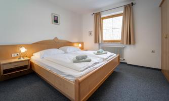 A cozy bedroom with a double bed and two pillows. Large windows provide plenty of daylight and an inviting atmosphere.