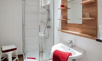 A modern bathroom with a glass shower and a sink. Red towels and a wooden shelf give the room an inviting atmosphere.