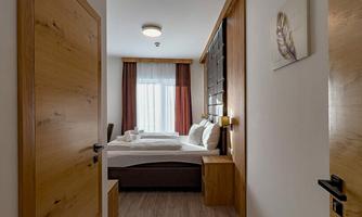 A cozy hallway with a limited view of a bedroom. The room is bright and furnished in a modern style, with wooden details and large windows.