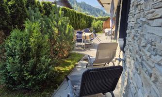 A cozy outdoor area with garden furniture and green plants. In the background, bare mountains can be seen.