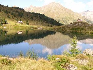 A quiet lake surrounded by mountains and forests. The landscape is reflected in the water.