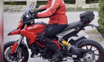 A man is riding a red Ducati motorcycle. He is wearing a helmet and a red jacket and is standing on a busy street.