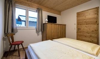 A cozy bedroom with two single beds and wooden interior. The room has a window, a television, and a wooden dresser.