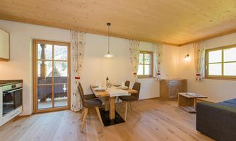 A cozy dining area with a wooden table and chairs. Large windows provide plenty of daylight in a bright room with a wooden-paneled ceiling.