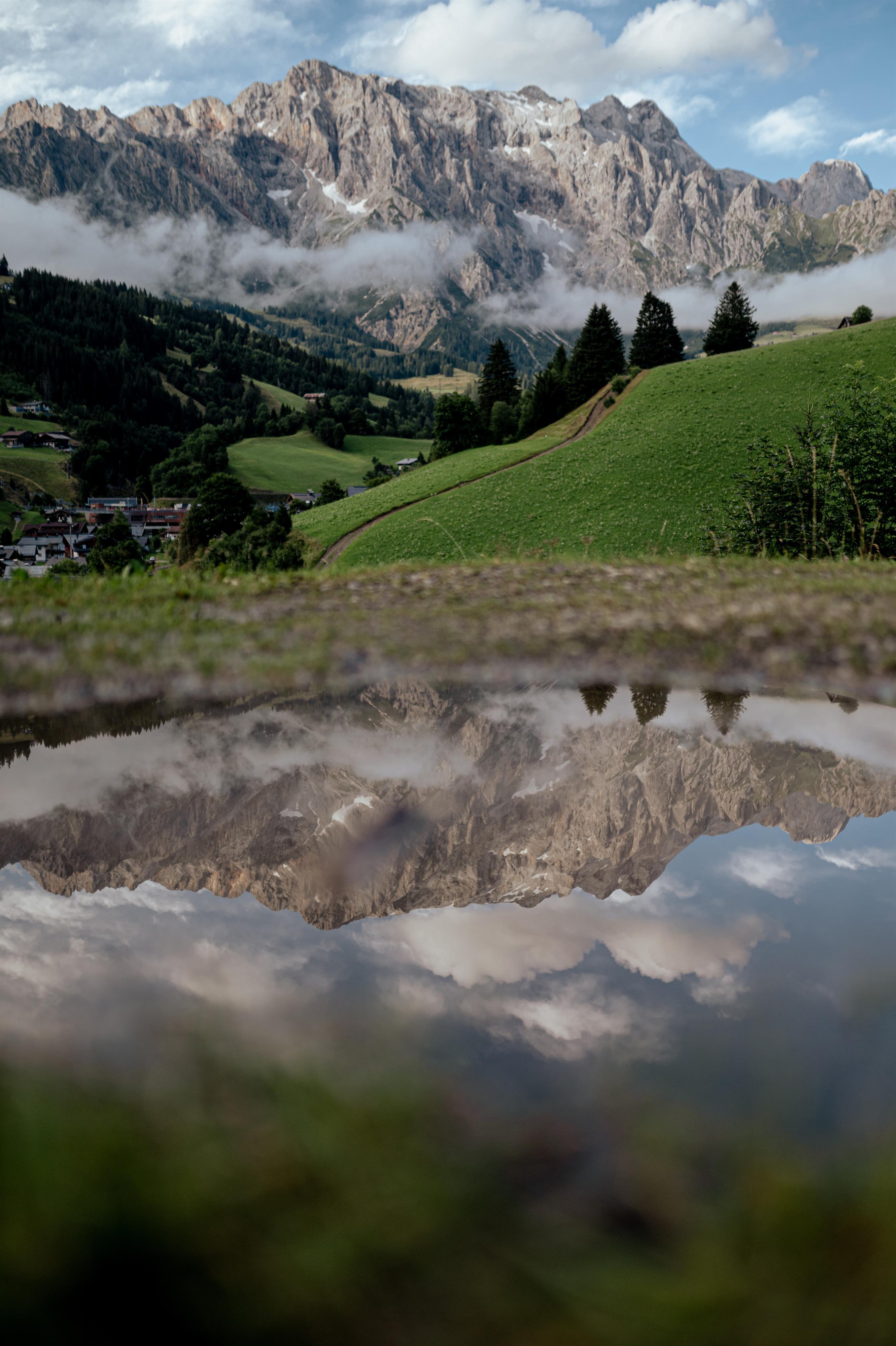 A beautiful mountain with green meadows and a clear sky. The reflecting mountains can be seen in the puddle of water.