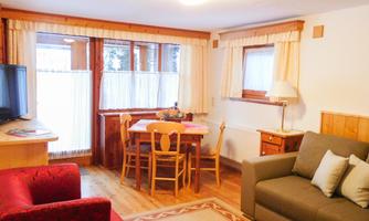 A cozy living space with a red sofa and a gray sofa. The room has a dining table with chairs and plenty of daylight through the windows.