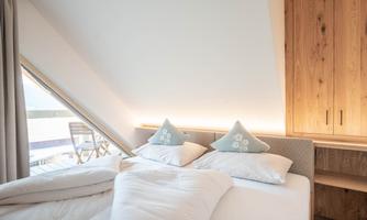 A cozy bedroom with a large window and a modern bed. The bright colors and wooden details create an inviting atmosphere.