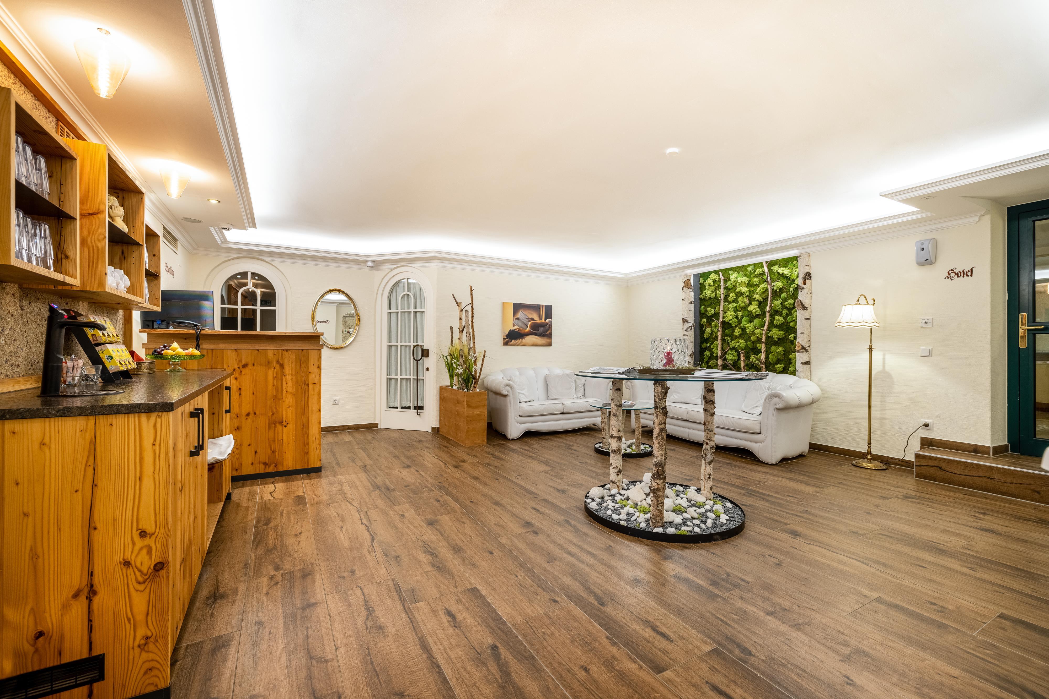 A cozy reception area with wooden shelves and warm lighting. The furnishings include a bright sofa landscape and plants for an inviting atmosphere.