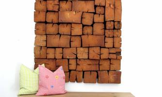 A rustic wooden panel with earthy colors hangs on the wall. In front, there is a wooden bench with two colorful cushions.