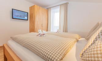 A cozy bedroom with two beds and checkered bedspreads. A television hangs on the wall, and the window lets in plenty of daylight.