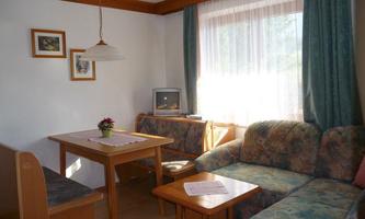 A cozy living space with a table and seating. The light falls through a large window and there are some decorative pictures on the wall.