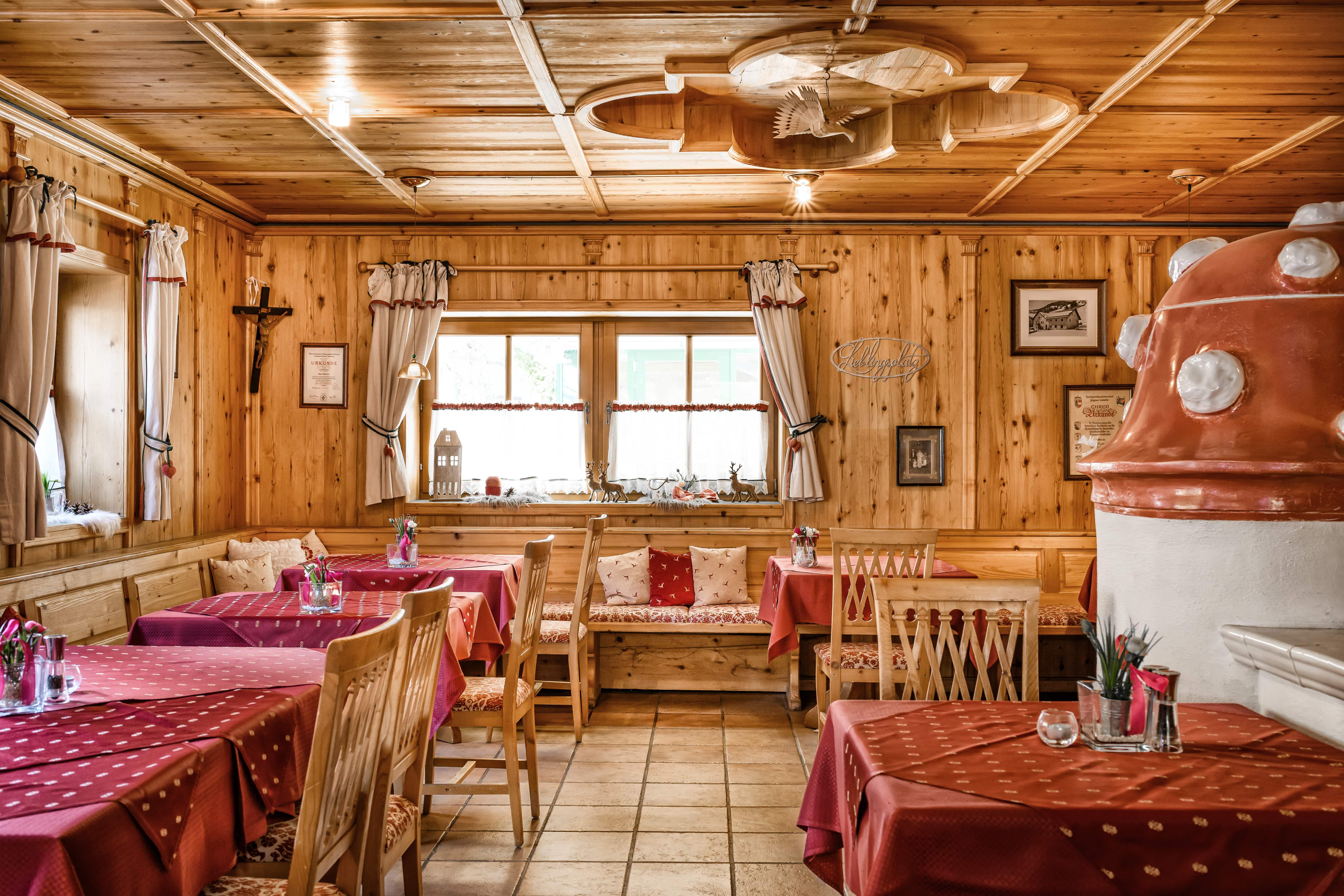 A cozy restaurant with wooden walls and tables covered in red. Large windows and decorative elements create an inviting atmosphere.