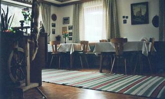 A cozy dining room with tables and chairs, decorated with plants and pictures. The floor is covered with a striped carpet.