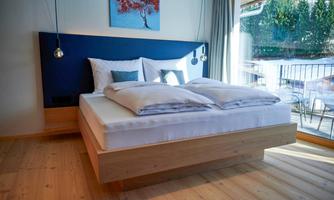 A modern bedroom with a comfortable bed and wooden floor. Large windows provide a view outside and let in plenty of light.