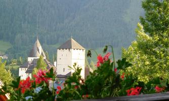 A picturesque castle with towers, surrounded by green mountains. In the foreground, colorful flowers are blooming.