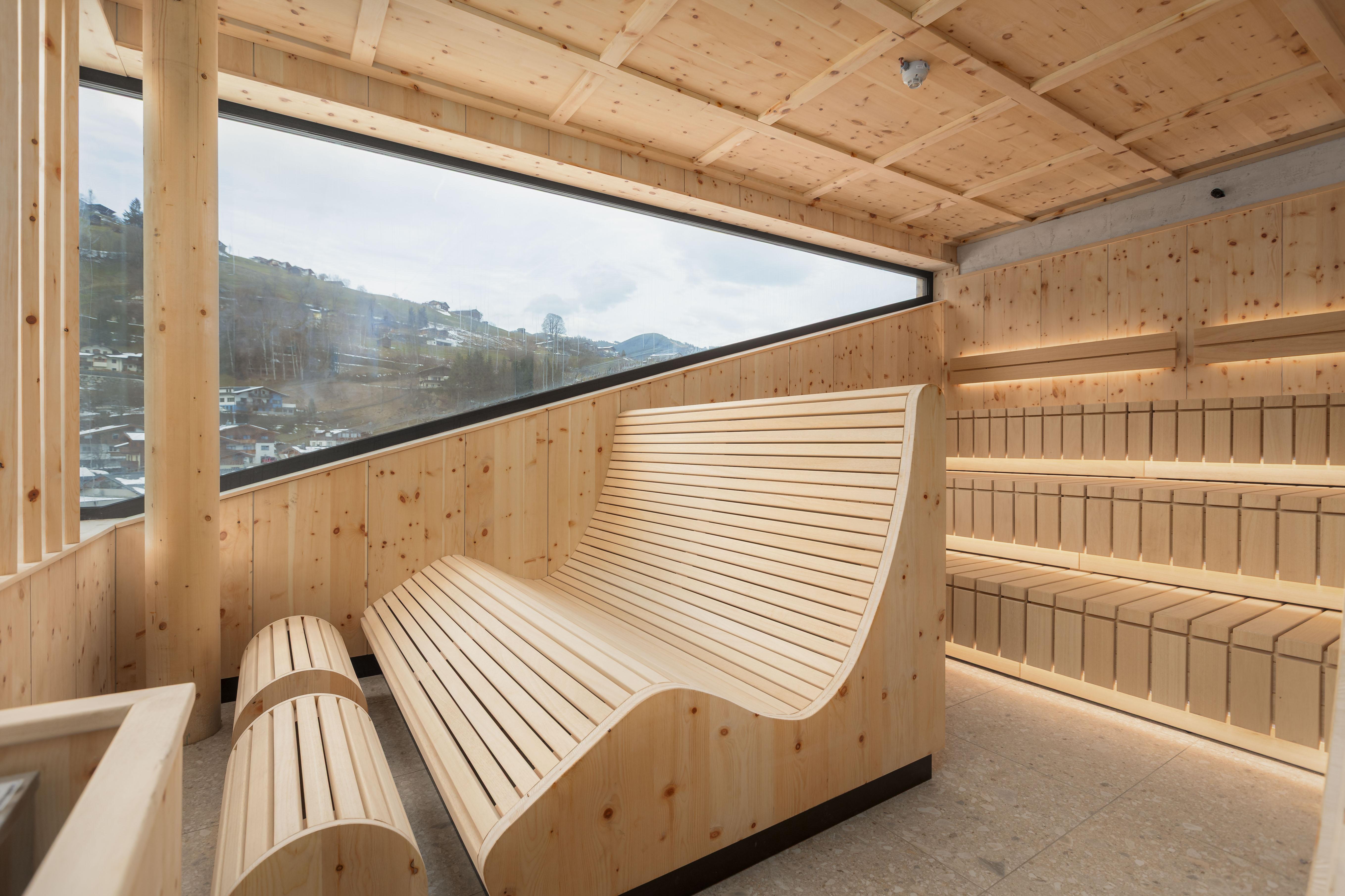 A modern, bright sauna room made of wood with large windows and a view of the mountains. The furniture is designed in a minimalist and inviting style.