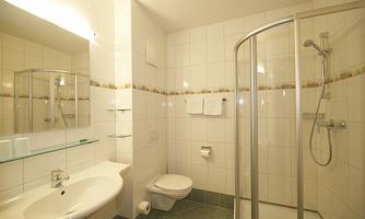 A modern bathroom with a shower and a sink. The walls are tiled in white and there is a large mirror.