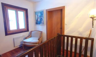 An inviting hallway with wood paneling and a cozy armchair. A window and a painting give the room a bright, friendly atmosphere.