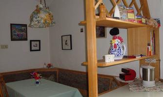 A cozy kitchen with a dining table and a wooden shelf. On the shelf, there is a teapot and some clever decorations.