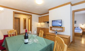 A cozy apartment with wooden furniture and a dining table. In the background, an integrated kitchen and a living area are visible.