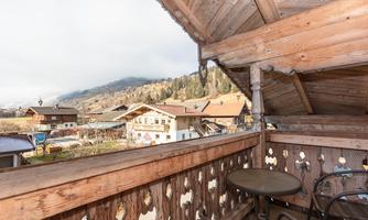 A balcony with a view of the mountains and traditional wooden houses. The landscape is calm and picturesque, typical of the Alpine region.