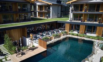 A modern hotel with a beautiful pool and an elegant terrace.  
Surrounded by green plants and cozy seating, the place invites relaxation.