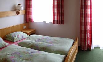 A simple room with two beds and colorful bedspreads. The windows are decorated with checkered curtains.