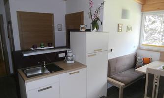 A modern kitchen corner with a small dining area. The bright decor and large windows create a pleasant atmosphere.