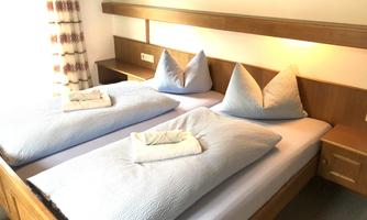 A cozy bedroom with two separate beds and blue bed linen. The furnishings are made of wood and create a warm atmosphere.