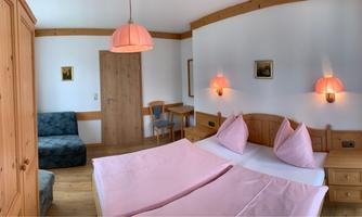 A bright bedroom with wooden furniture and a large double bed. The walls are painted in neutral colors, and there is a cozy seating area.