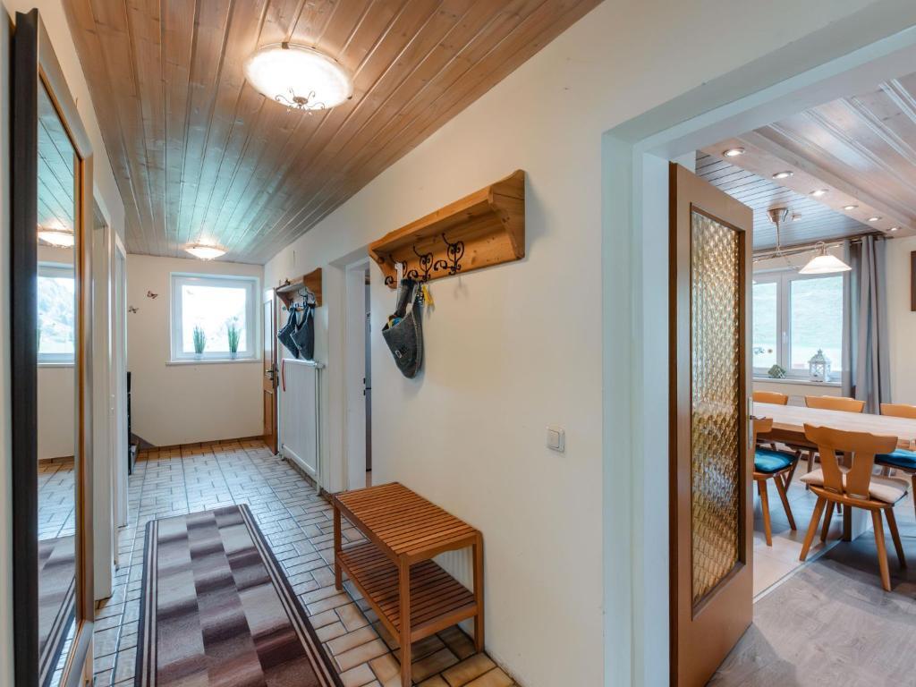Bright hallway with tiled floor, wooden ceiling, wardrobe with hooks and bench, and access to the dining area with a large dining table and chairs.