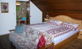A cozy bedroom with a double bed and a rustic wooden wall. In the background, a bathroom is visible.