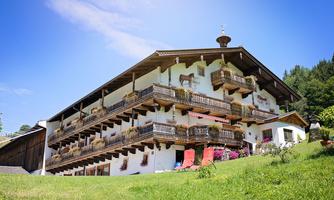 A traditional alpine house with balconies and colorful flowers. Surrounded by green meadows and blue sky.